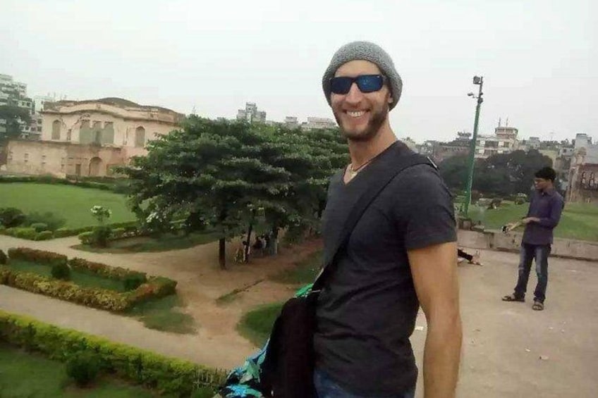 Una persona parada en un área pavimentada, con un parque y edificios al fondo. 4