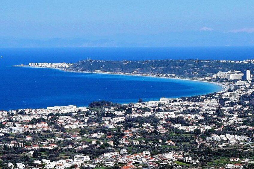 A coastal cityscape with a clear blue sea, dense residential buildings, and a hilly terrain in the background. 5