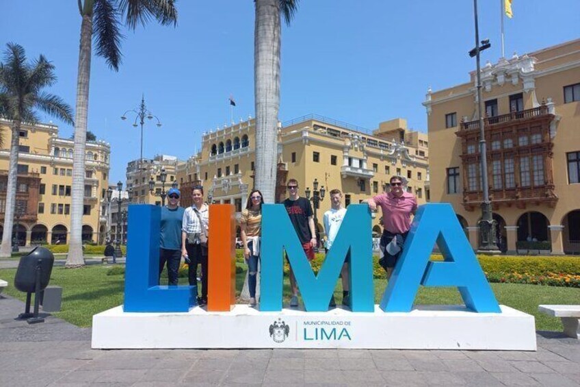Un grupo de personas de pie frente a grandes letras azules que deletrean 'LIMA', con un emblema de la ciudad debajo. 5