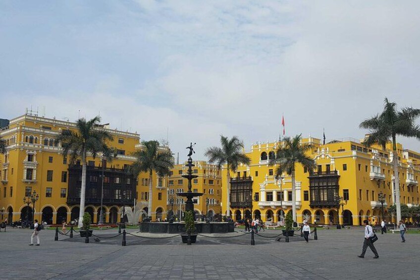 Una plaza con edificios amarillos, palmeras y una fuente. 1