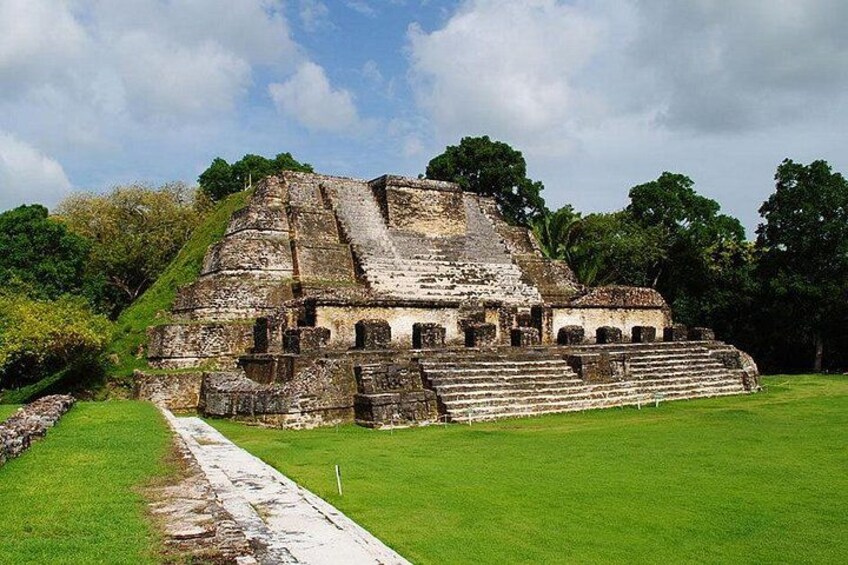 A large ancient pyramid with stepped terraces and a surrounding grassy area. 1