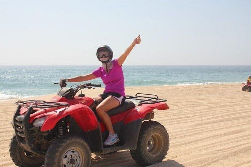 A person riding a red ATV on a sandy beach with the ocean in the background. 1