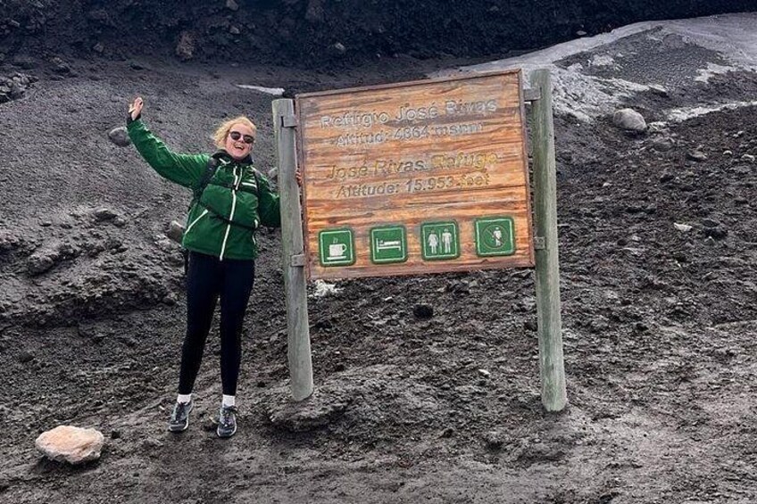 Eine Person steht neben einem hölzernen Wegweiser mit Wandermarkierungen und Beschriftung. 2