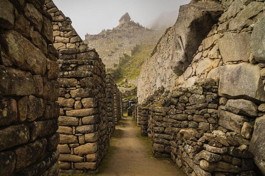 A stone pathway leading through ancient ruins with stone walls and a mountain in the background. 4