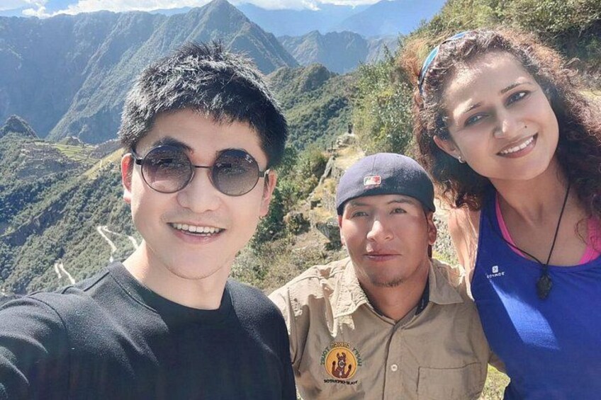 Three people standing on a mountain with a view of a winding road and mountains in the background. 2