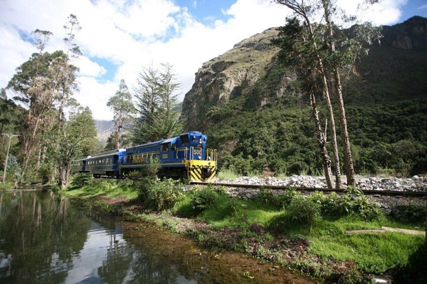 A blue train on tracks beside a river, surrounded by greenery and mountains. 5