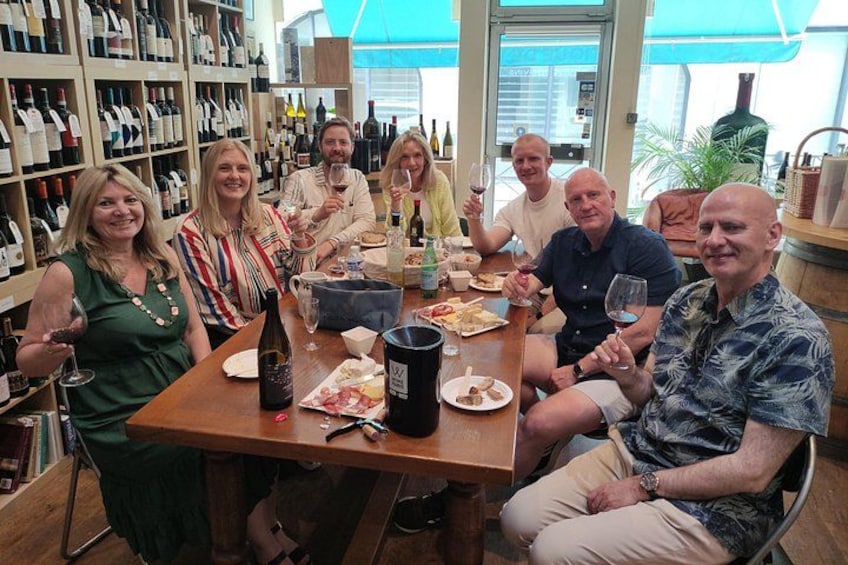 A group of people sitting around a table with wine bottles and glasses. 2