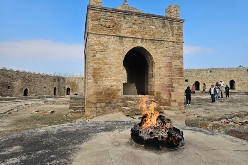 A stone archway with a fire in front, surrounded by ruins and visitors. 5