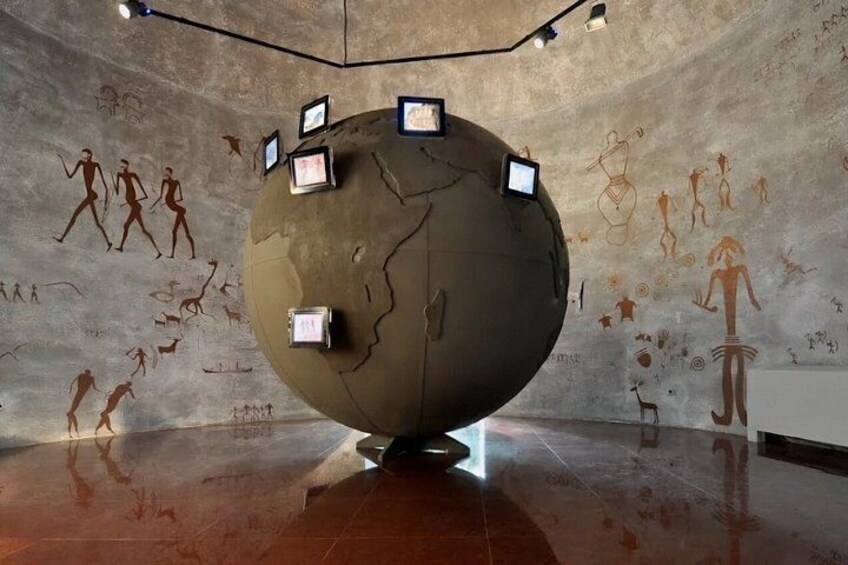 A large spherical sculpture with projections, surrounded by cave paintings on the walls. 5