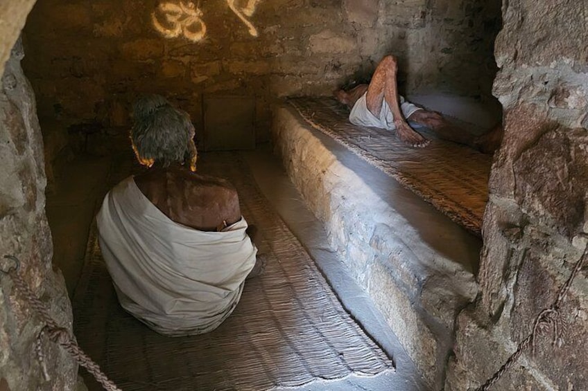 A person sitting on a stone bench in a cave-like structure with a rough wall and a small step leading up to the bench. 3