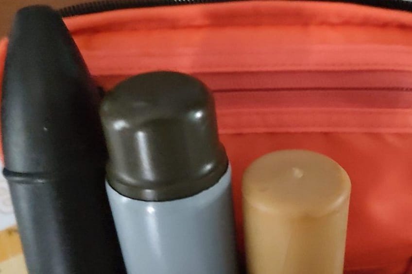Una borsa rossa con tre oggetti cilindrici: un oggetto nero, un oggetto grigio e un oggetto beige. 2