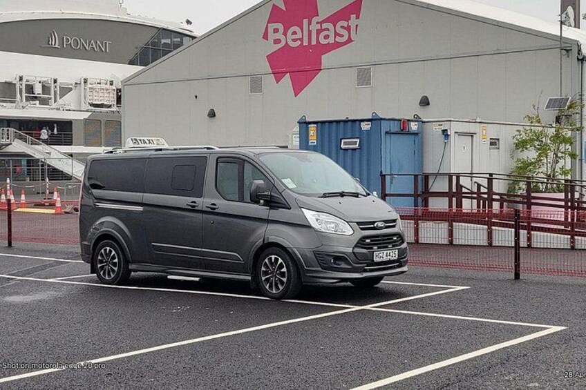 Un furgone grigio parcheggiato in un parcheggio, con un grande edificio sullo sfondo con la scritta 'Belfast'. 4