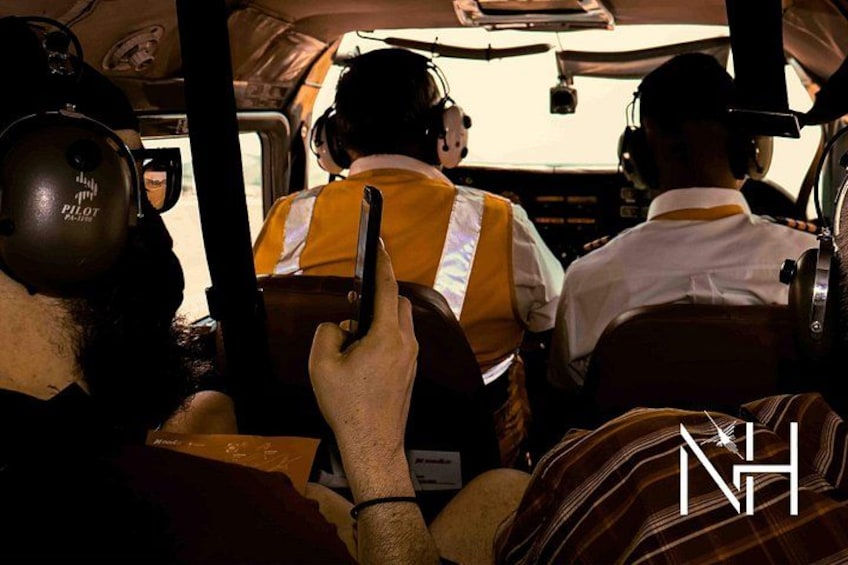 A cockpit with pilots wearing headsets and a person holding a mobile phone. 3