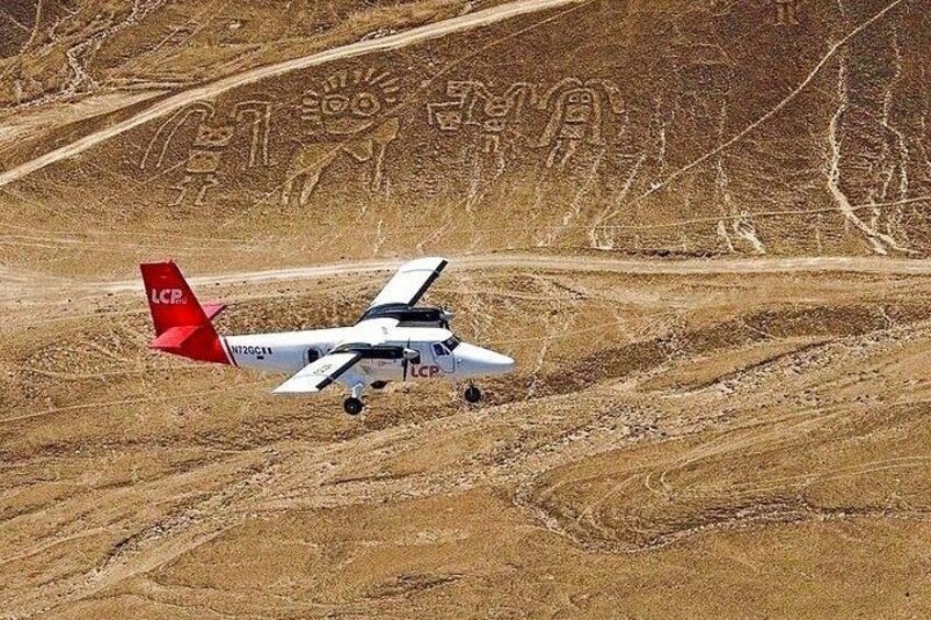 A small aircraft with a red tail and the letters 'LCP' on its side, taxiing on a dirt runway with a mountainous landscape in the background. 1