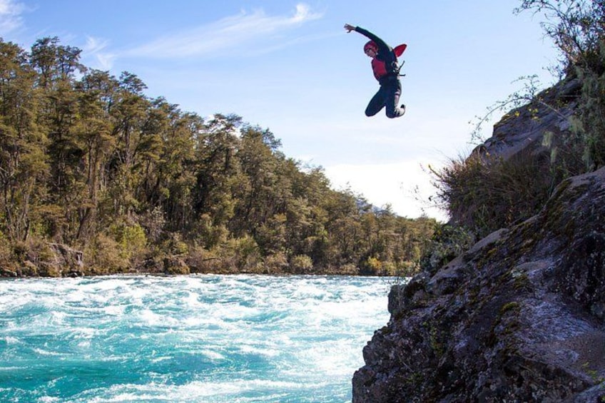A person performing a jump off a cliff into a river surrounded by trees. 4