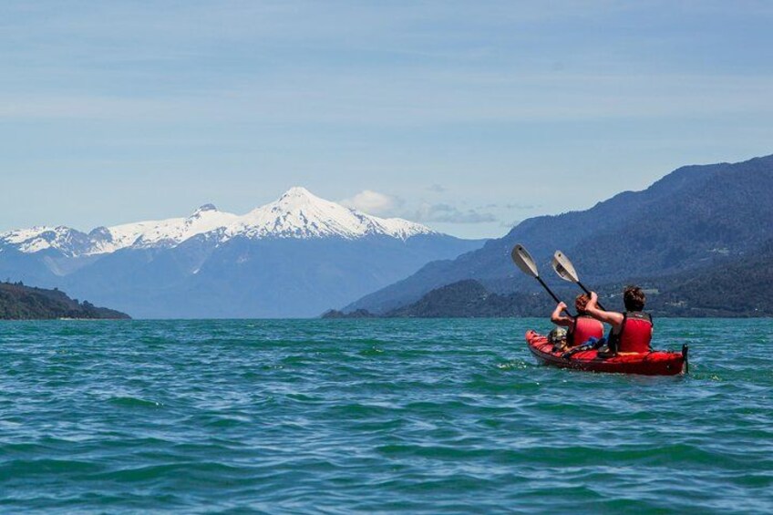 Two people kayaking on a calm lake with snow-capped mountains in the background. 1