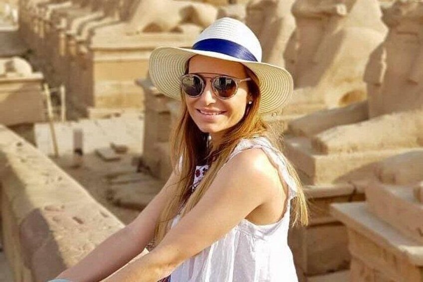 A person wearing a white sleeveless top and a wide-brimmed hat, standing in front of ancient stone ruins. 1