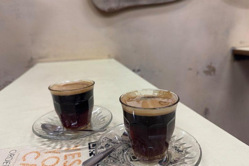 Two glasses of dark liquid on a white table with a spoon. 2