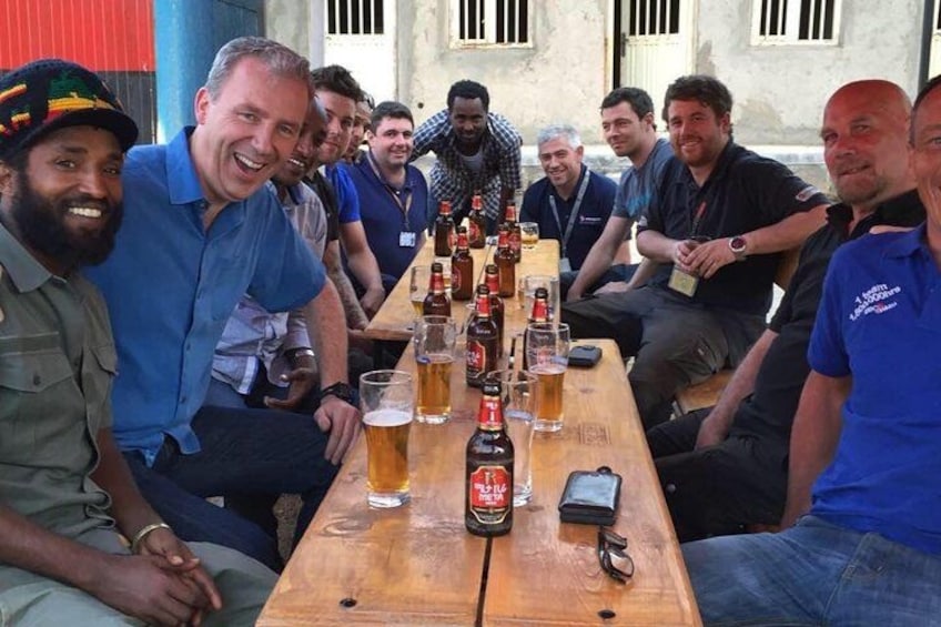 A group of people sitting around a wooden table with bottles of beer and glasses. 5