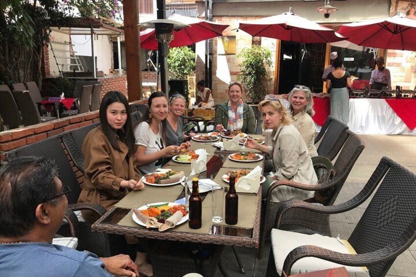 A group of people dining outdoors at a restaurant with wicker chairs and red umbrellas. 4