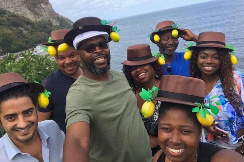 Un grupo de personas con sombreros de limones, de pie junto a una masa de agua con un acantilado al fondo. 1
