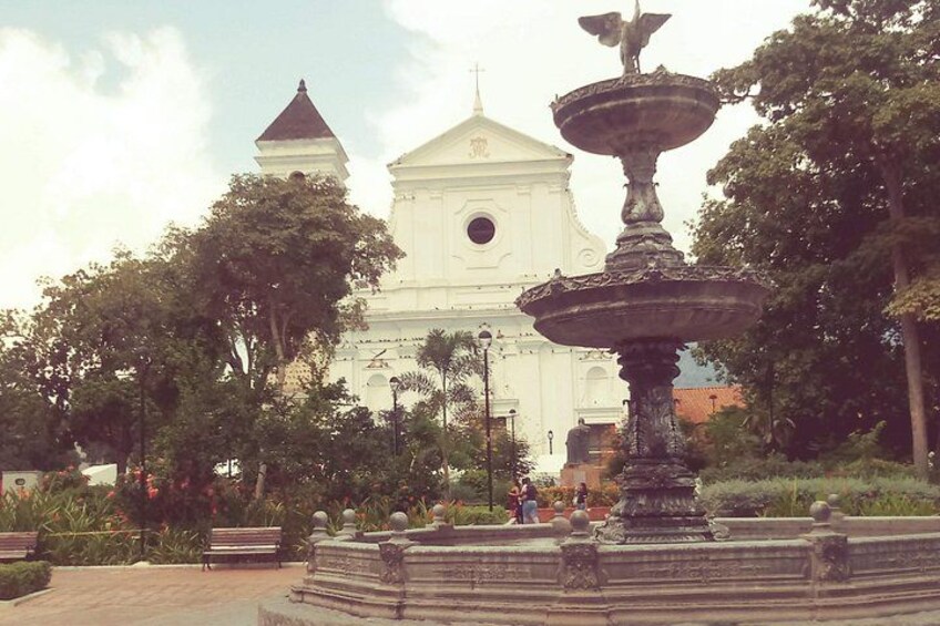 Una iglesia blanca con un campanario, rodeada de árboles y una fuente. 4
