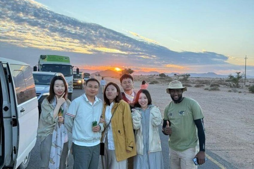 A group of people standing on a dirt road with a sunset in the background. 1