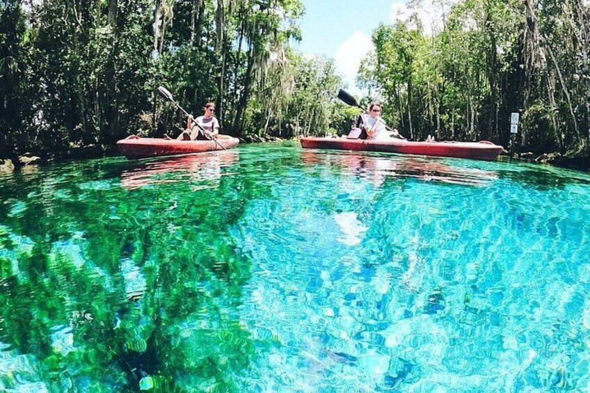 Dos personas hacen kayak en un río azul y transparente, rodeado de árboles. 5