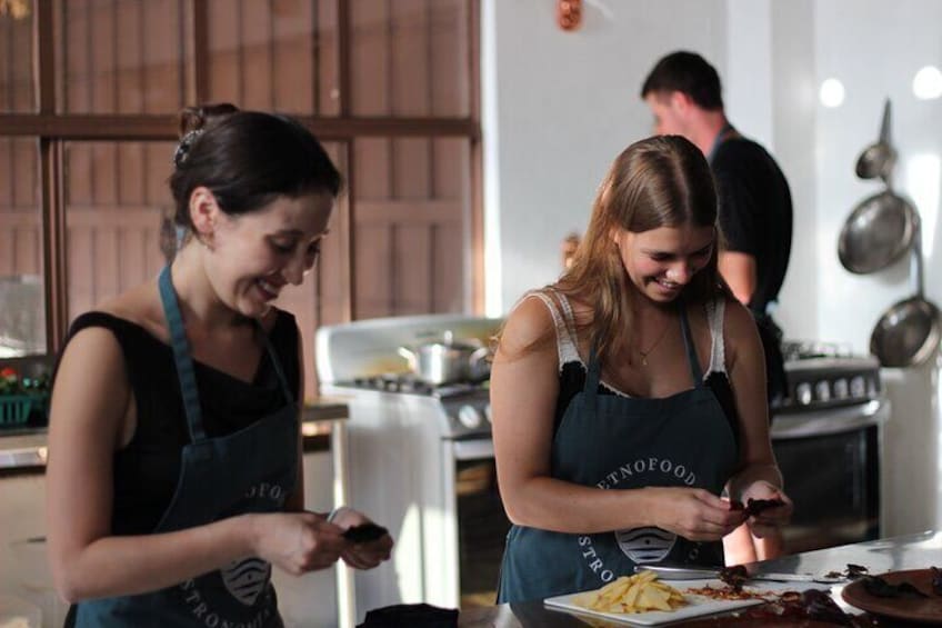 Two individuals in a kitchen, one cutting cheese and the other preparing food. 3