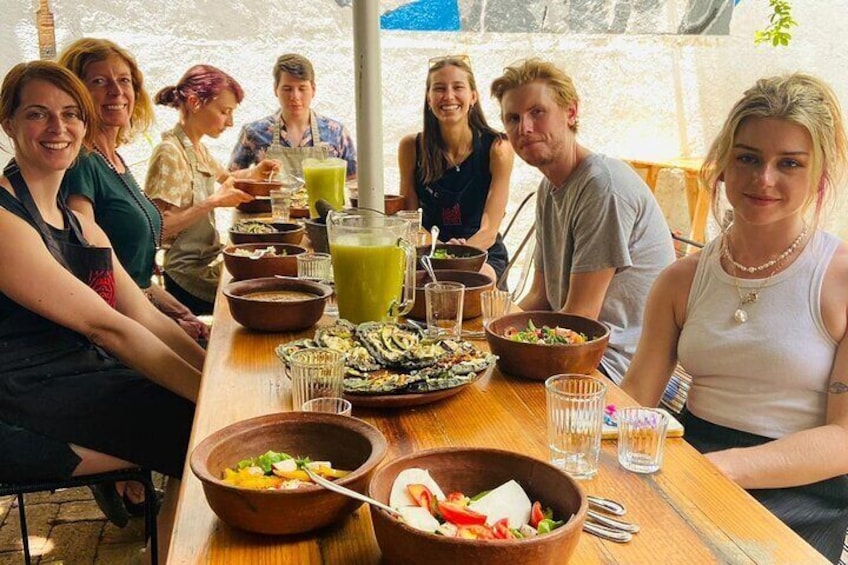 A group of people sitting around a wooden table with various dishes and drinks. 1