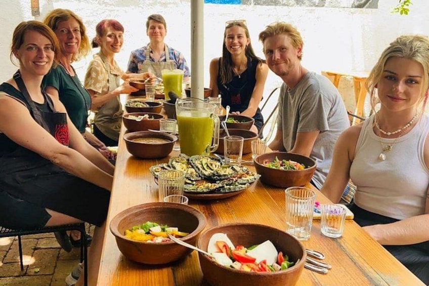 A group of people sitting around a wooden table with various dishes and drinks. 2