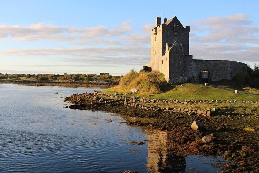 A historic stone castle by a calm river with a grassy mound and a clear sky. 1