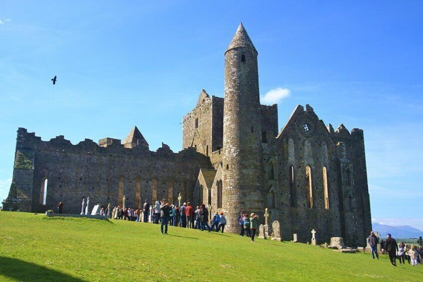 A historic castle with a prominent tower, surrounded by a grassy area with visitors. 2