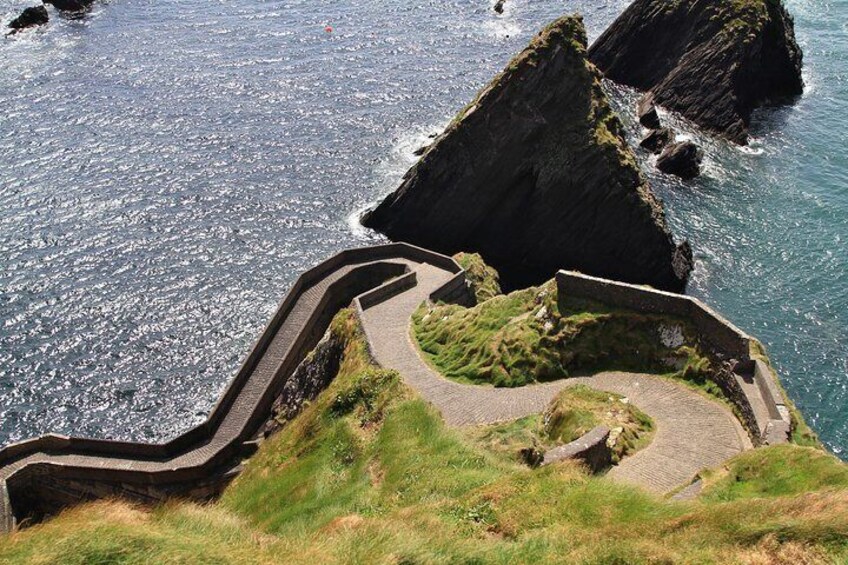 A coastal cliff with a winding stone pathway and a rocky outcrop. 5