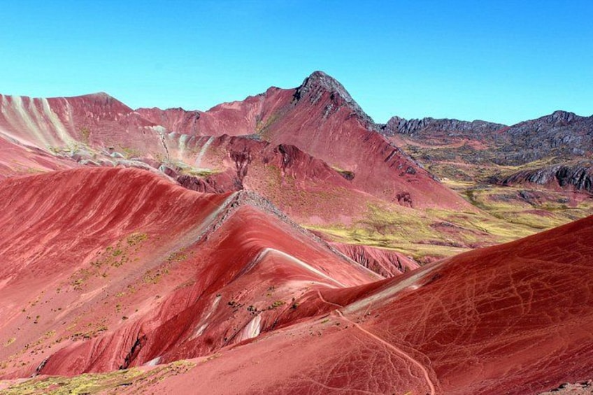 Un paisaje montañoso y escarpado con tonos rojos y amarillos, cielo despejado y un camino sinuoso. 2
