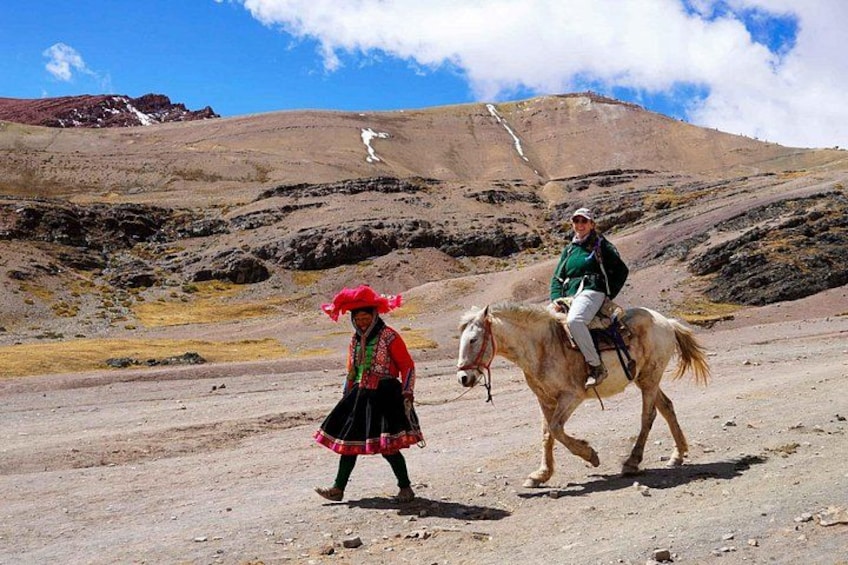 A person riding a horse on a dirt path with a mountainous background. 2