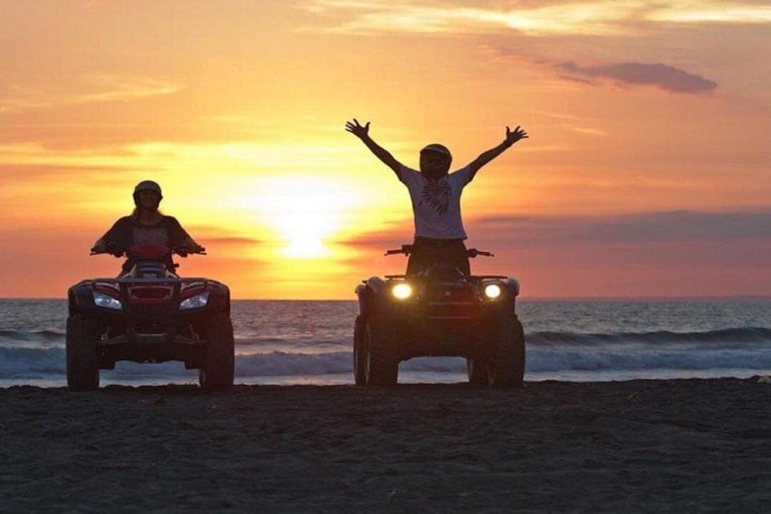 Two people on ATVs facing the sunset on a beach. 4