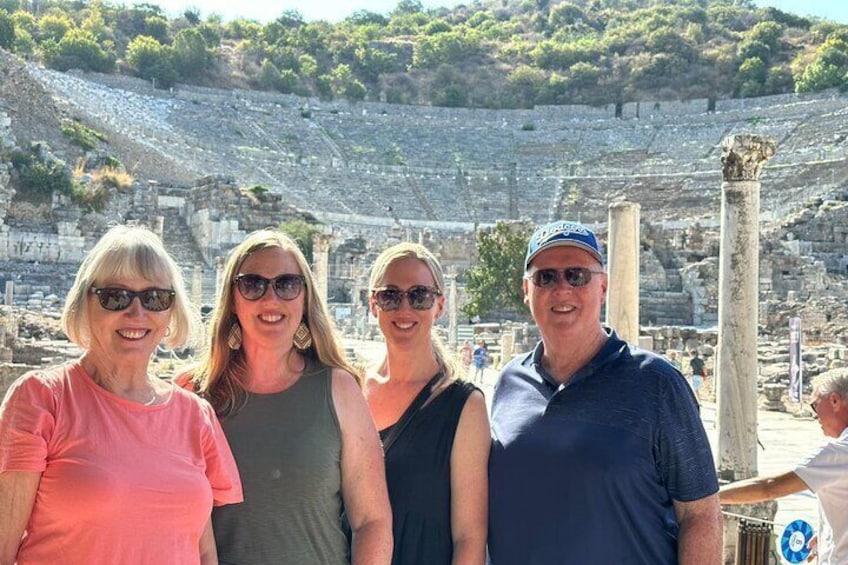 A group of people standing in front of an ancient amphitheater with stone columns and a tiered seating area. 2