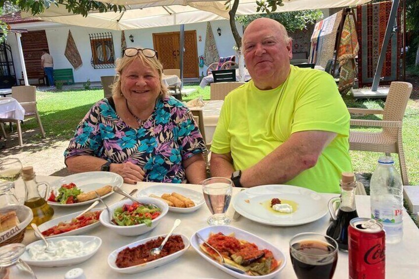 Two people seated at an outdoor table with various dishes and drinks. 2
