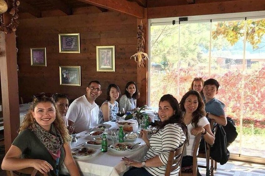 A group of people seated around a table with food and drinks, in a wooden room with framed pictures on the wall. 3