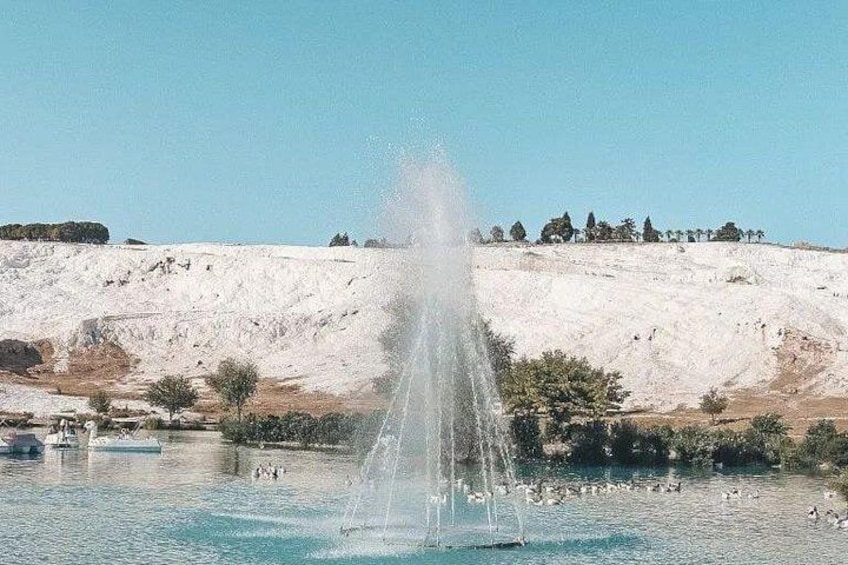 A fountain in a body of water with a hilly landscape in the background. 3