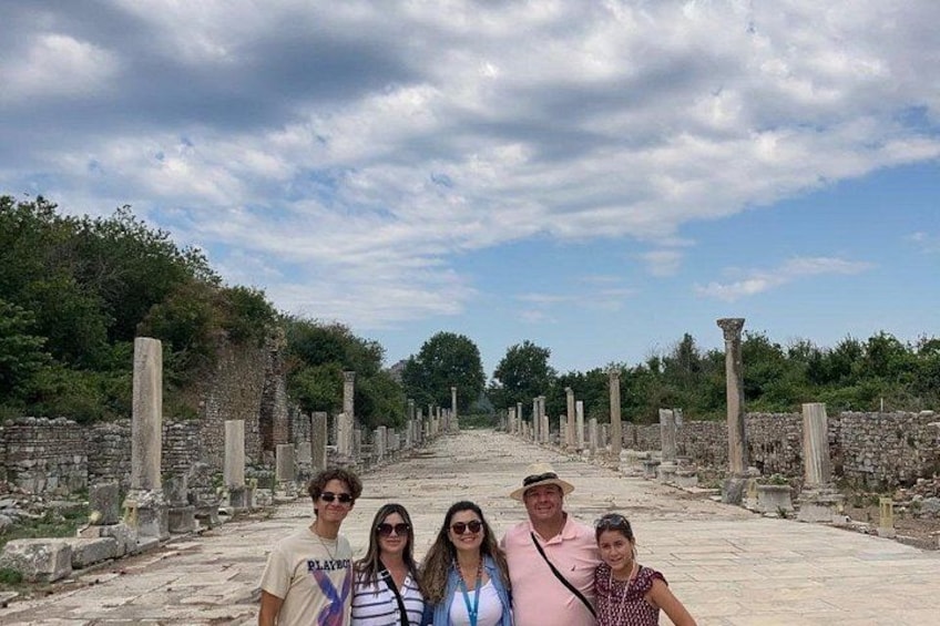 A group of people standing on an ancient stone pathway with columns on either side, surrounded by greenery and ruins. 5