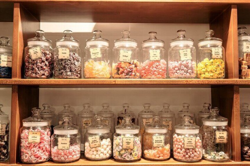 Une étagère en bois sur laquelle sont disposés plusieurs bocaux en verre remplis de différents types de bonbons. 2