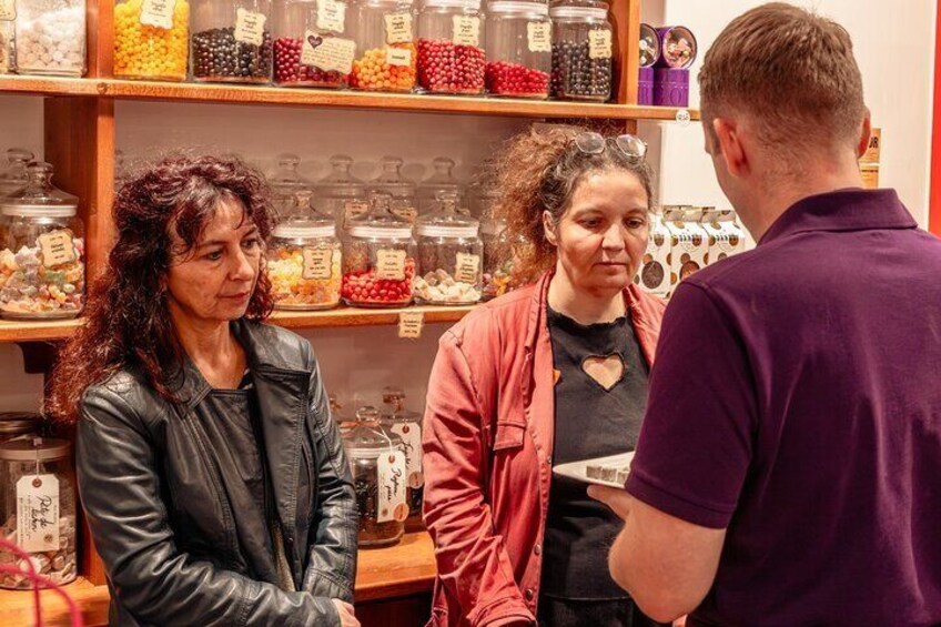 Trois personnes se trouvent dans un magasin, devant des étagères remplies de bonbons de toutes les couleurs. 4