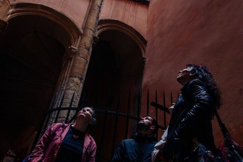 A person in a black jacket looking up at a tall, arched doorway in a narrow alleyway. 2
