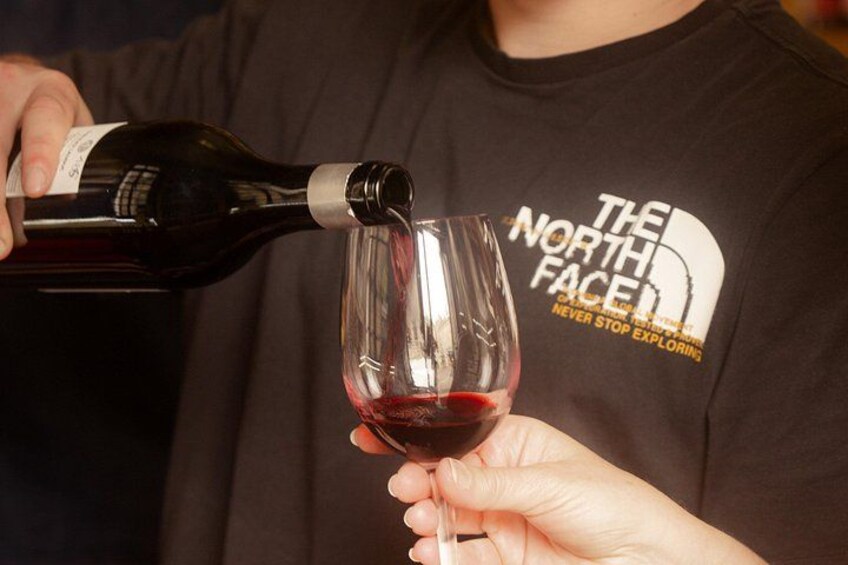 A person pouring red wine from a bottle into a glass. 2