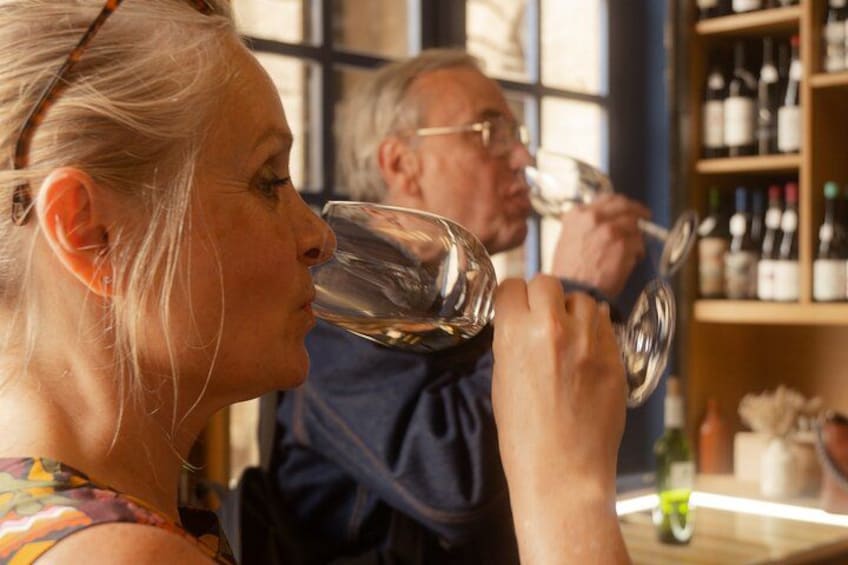Two people tasting wine in a room with shelves of wine bottles. 1