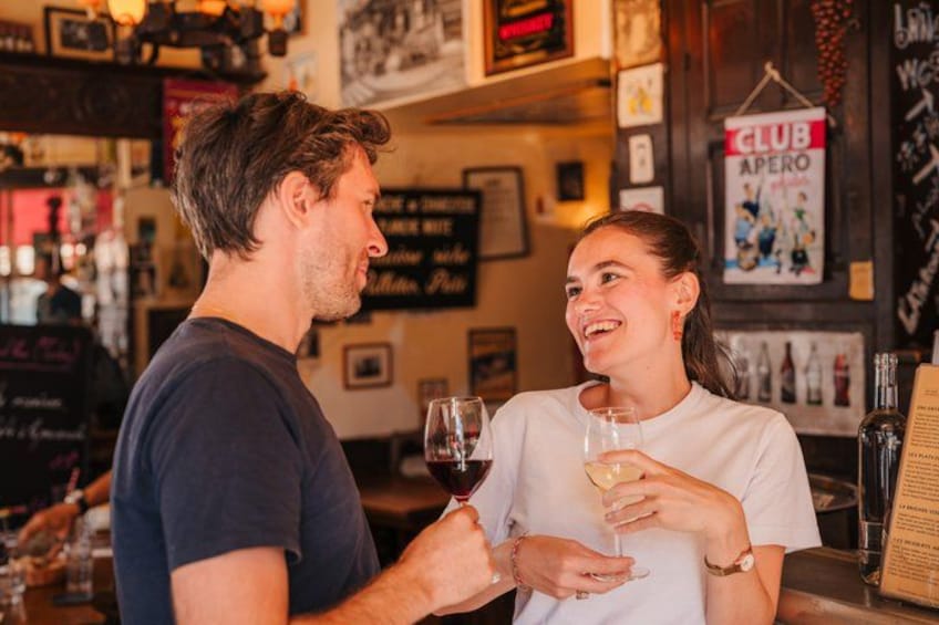 Une personne tenant un verre de vin, une autre personne tenant un verre d’eau, et un comptoir de bar avec des bouteilles et un menu. 1
