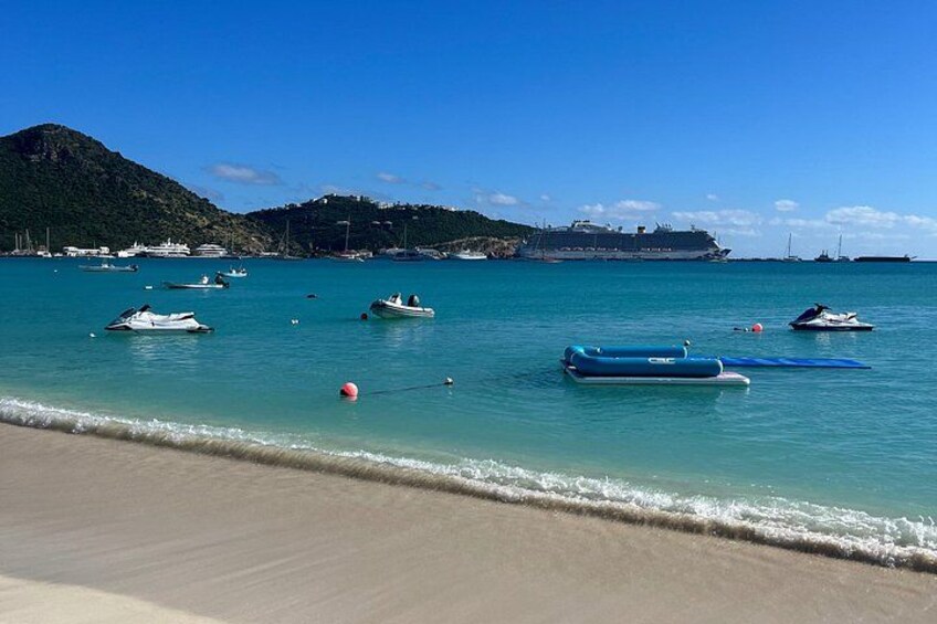 Una playa con barcos, un gran crucero y montañas al fondo. 4