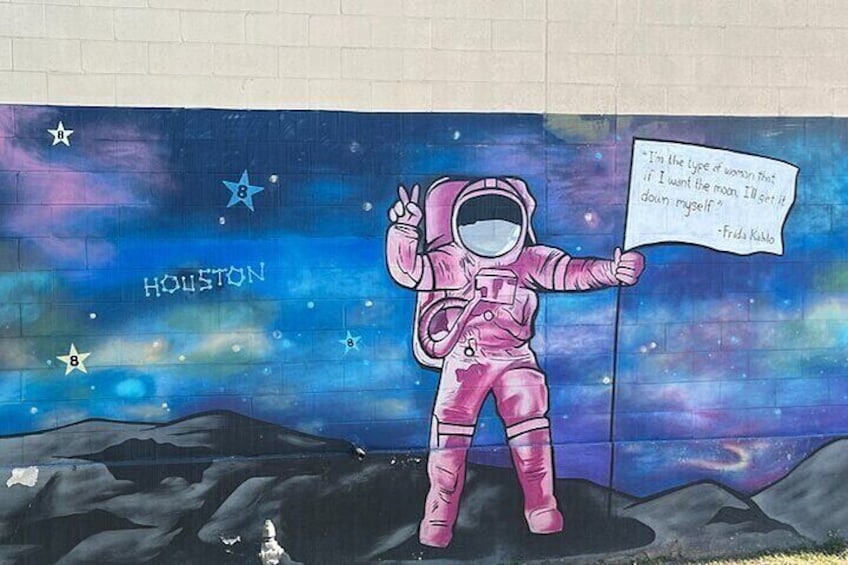 A mural of an astronaut holding a sign with a quote, set against a starry night sky background with the word "Houston" visible. 3